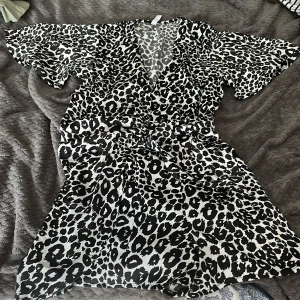 Leopardmönstrad kortklänning från new yorker - Snygg kortklänning från H&M med svartvitt leopardmönster. Klänningen har v-ringning, vida korta ärmar och markerad midja med knytband. Perfekt för dig som vill sticka ut med en trendig look. Inbyggda shorts men ser ut som en klänning❤️