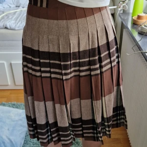 Rutig kjol - Rutig, veckad kjol i olika nyanser av brunt. Ungefär knälängd och saknar lapp men är runt 35cm i midjan och 62,5 i längd. Köpt på Beyond Retro