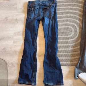 Blå bootcut jeans från Gina Tricot - Snygga blå jeans från Gina Tricot i klassisk bootcut-modell. Jeansen har kontrastsömmar, fem fickor och gylf med dragkedja och knapp. Perfekta för dig som gillar en tidlös look med lite utsvängda ben.