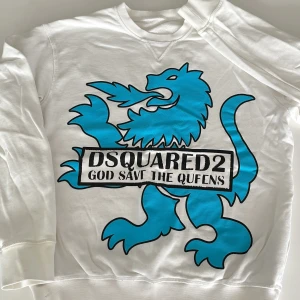 Vit sweatshirt från Dsquared2 med blått lejon - Cool vit sweatshirt från Dsquared2 med stor blå lejonprint och texten 'God Save The Queens' framtill. Tröjan har rund halsringning och ribbade muddar. Perfekt statement piece för dig som vill sticka ut med en unik design.