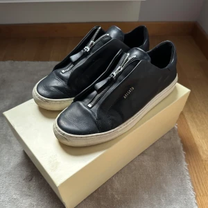 Svarta sneakers från Axel Arigato - Svarta sneakers från Axel Arigato med dragkedja framtill. 