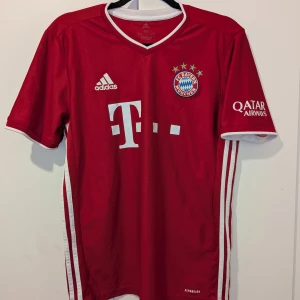 Röd FC Bayern München fotbollströja från Adidas - Säljer en röd FC Bayern München fotbollströja från Adidas med korta ärmar. Tröjan har vita detaljer och logotyper på framsidan samt texten 'FC Bayern München' på baksidan. Perfekt för fans av laget! Använde den några gånger men sen den passa inte längre. Den är lite sliten vid bild 3 men annars i perfekt form, man märker inte ens den. Kan diskuteras om ett bra pris! Äkta från Tyskland!