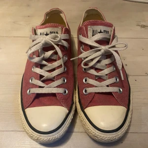 Röda/Rosa Converse All Star sneakers - Säljer ett par röd/rosa Converse All Star sneakers med vita snören och tåhätta. Skorna köptes i usa i butik och har knappt blivit använda. Jag väljer att sälja dem här då min farmor gav mig dem men det är inte riktigt min stil. Skorna har inga skador och är lite gula i sulan pga att dem är några år gamla. 