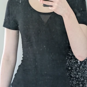 Svart tight topp med meshdetaljer - Snygg svart compression tröja, gjord för att hålla axlarna bakåt för en rackare rygg. Toppen har en tight passform som framhäver figuren. 