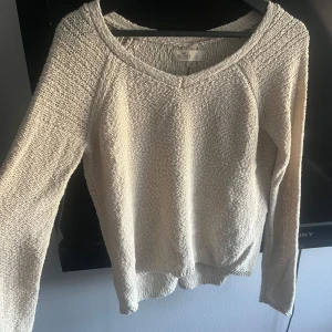 Beige stickad tröja från Hollister - Säljer en snygg beige stickad tröja från Hollister. Tröjan har en v-ringad hals och långa ärmar. Baksidan har en cool snörningsdetalj som ger en unik touch. Perfekt för våren!