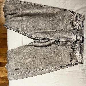Grå jeans med lös passform - Säljer ett par grå jeans med en avslappnad, lös passform. De har en klassisk femficksdesign och en knapp gylf framtill. Perfekta för en casual look.Storlek 30/32