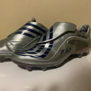 Adidas F50 fotbollsskor i silver ”Lionel Messi” - Adidas sällsynta F50 fotbollsskor i silverfärg med mörkblå detaljer i storlek 42 2/3. De kommer med nya utbytbara dobbar och verktyg för justering. Både plast och metalldobbar, för konstgräs och gräsplaner! Skorna är använda men i mycket bra sick (se bilder). Hör av dig vid eventuella frågor!