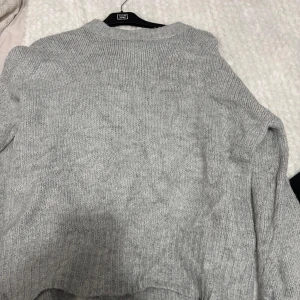 Grå stickad tröja från 157 - Säljer en mysig grå stickad tröja från 157. Perfekt för kyliga dagar med sin mjuka och bekväma passform. Tröjan har långa ärmar och en klassisk rund halsringning. Ett måste i garderoben för en stilren look. 