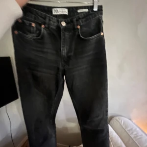 Svarta jeans från Zara - Snygga svarta jeans från Zara med klassisk femficksdesign. De har en knappgylf och är perfekta för en stilren look. Passar bra till både vardag och mer uppklädda tillfällen.