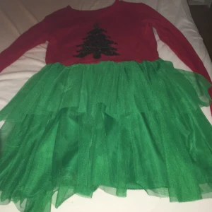 Röd och grön klänning med paljetter - Säljer en festlig klänning i rött och grönt med en paljettprydd julgran på bröstet. Klänningen har långa ärmar och en volangkjol i grönt tyll. Perfekt för julens alla festligheter! 🎄✨🎅