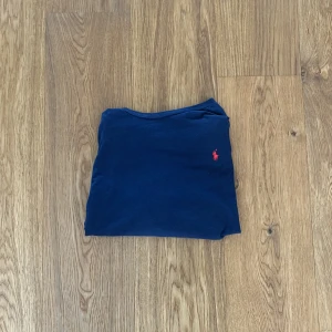 Mörkblå långärmad tröja från Ralph Lauren - Säljer en stilren mörkblå långärmad tröja från Ralph Lauren med den röda loggan på bröstet. Perfekt för en avslappnad och snygg look. Perfekt för alla årstider och tveka inte av att höra av er vid funderingar! 