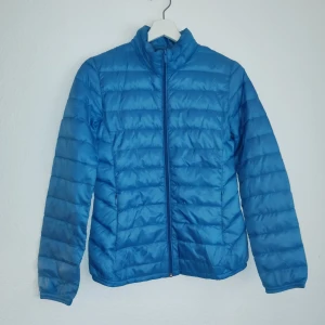 Blå dunjacka från C - Säljer en superlätt blå dunjacka från C. Jackan har en dragkedja framtill och är quiltad för extra värme. Perfekt för kyliga dagar när du vill hålla stilen enkel och bekväm.