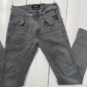 Replay Anbass - Snygga grå jeans från Replay med en klassisk femficksdesign. De har en knappgylf och bälteshällor, vilket gör dem perfekta för en avslappnad stil. Jeansen har en modern passform och är tillverkade i ett bekvämt material. Slitage syns på sista bilden annars är de fint skick