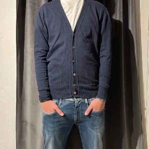 Mörkblå kofta  - Säljer en klassisk mörkblå kofta. Den har en v-ringning och knappar framtill samt två praktiska fickor. Perfekt för lager-på-lager under kyligare dagar.