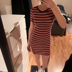 Randig kortklänning - Säljer en snygg randig kortklänning i vinrött och rosa. Klänningen har en tight passform och korta ärmar. Den är gjord i ett mjukt och bekvämt material och är väldigt stretchig💕 Jag är 170cm för referens