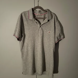 Grå pikétröja från Moncler - Snygg grå pikétröja från Moncler med klassisk krage. Kan passa bra till sommaren. Storlek medium och jätte fint skick