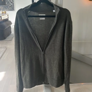 Grön cardigan från these glory days - Säljer en skitsnygg grön cardigan från These Glory Days i Superior Merino. Koftan har en dragkedja framtill och långa ärmar, perfekt för kyligare dagar. Den är tillverkad i ett mjukt och bekvämt material som ger en lyxig känsla. Den är i väldigt bra skicka och inga defekter finns👍👍 storlek L men sitter som M