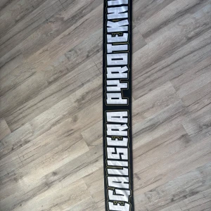 Svart och vit halsduk med text - Säljer en svart halsduk med stora vita bokstäver och gul kant. Texten på halsduken är iögonfallande och perfekt för att visa ditt stöd. Passar bra för sportevenemang och attityd.