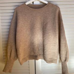 Beige stickad tröja - Säljer en mysig beige stickad tröja med rund hals och långa ärmar. Tröjan har ribbade muddar vid ärmslut och nederkant, vilket ger en stilren look. Perfekt för kyligare dagar!