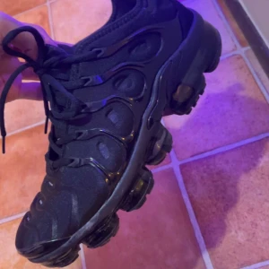 Svarta sneakers från Nike - Snygga svarta sneakers från Nike med en futuristisk design och robust sula. Skorna har snörning och en unik struktur på ovandelen som ger en cool look. Perfekta för både vardag och träning.