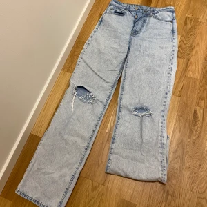 Ljusa jeans med slitningar - Säljer ett par ljusa jeans med slitningar. De har en knappgylf och är i en avslappnad, vid/straight passform. Passa mig bra i längden som är 174cm