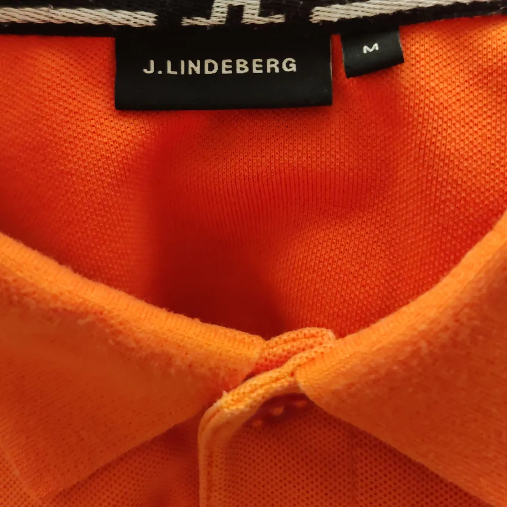 Snygg orange pikétröja från J.Lindeberg. Perfekt för en stilren och avslappnad look. Tröjan har en klassisk krage och knappar framtill. Passar utmärkt för både vardag och fritid.. T-paidat.