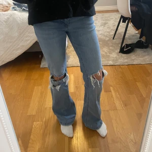 Blå jeans med slitningar - Snygga blå jeans med stora slitningar på knäna. De har en bootcut-stil som ger en avslappnad look. Perfekta för en trendig vardagsstil.Inga tecken på användning   Kan skicka mer bilder det är bara att skriva På hemsidan är de slut och köpta för runt 799kr inklusive frakt 🚚  Väldigt stretchiga så skulle passa de som bär 36 Själv är jag 165cm Brukar ha storlek 36 till 34 Midja tvärs över 38cm Ben 79cm  #copenhagenstyle #stockholmstyle #stockholmstil