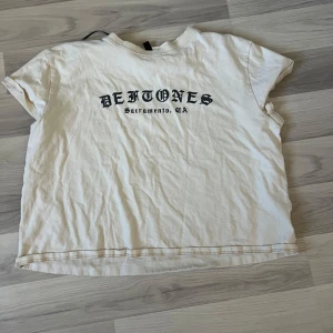Vit Deftones t-shirt  - Vit t-shirt från H&M Divided med svart Deftones-print på bröstet och texten 'Sacramento, CA'. Klassisk rund hals och korta ärmar. Materialet är mjuk bomull och modellen är normal passform. Perfekt för dig som gillar bandmerch och vill ha en chill stil.