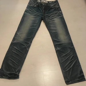 Mörkblå jeans från C-Brand - Snygga mörkblå jeans från C-Brand med coola slitningar och kontrastsömmar. Klassisk femficksmodell med tryckt insida i midjan och detaljerade bakfickor. Jeansen har rak passform och är tillverkade i robust denim som ger en schysst streetkänsla.