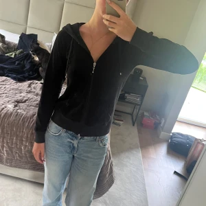 Svart kofta med dragkedja - Svart kofta i mjukt material med huva och snörning. Tröjan har dragkedja framtill, två fickor och långa ärmar. Perfekt för chill dagar och enkel att matcha med jeans eller mjukisbyxor. Snygg och skön passform som ger en avslappnad vibe. Alla kläder tvättas innan de skickas!
