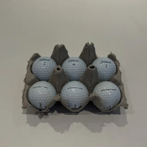 Titleist - Bilderna visar sex golfbollar av märket Titleist Pro V1, några med tryck som DHL och olika siffror. Det finns ingen bok på bilderna, endast sportutrustning. Ingen information om boktitel, författare eller innehåll kan utläsas.