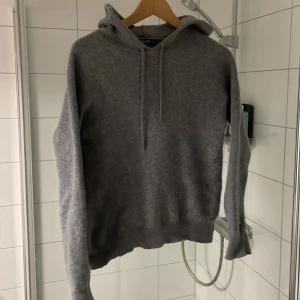 Grå hoodie från Tiger of Sweden - Mjuk och stilren grå hoodie från Tiger of Sweden i storlek M. Tröjan har huva med snörning och långa ärmar, tillverkad i ett stickat material som känns riktigt skönt mot huden. Perfekt för dig som gillar enkel och clean look. Sitter som S