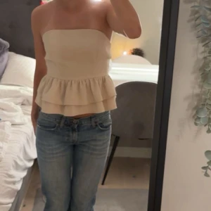 Beige volang bandeau tubtopp - Säljer en beige bandeau tubtopp med dubbla volanger nedtill och snygg knytning i ryggen. Den är köpt här på Plick men är ursprungligen ifrån SHEIN 