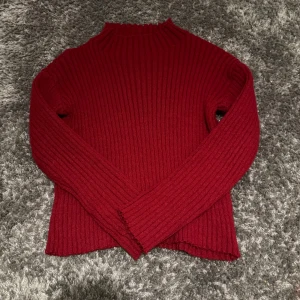 Röd ribbad stickad tröja  - Säljer en snygg röd stickad polotröja med ribbad struktur och lång ärm. Tröjan har en hög hals med vågig kant och är stickad i ett mjukt material som känns skönt mot huden. Perfekt för dig som gillar enkel men stilren design. Inte använd 
