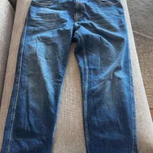 Replay Sandot relaxed tapered jeans 32 - Säljer ett par Replay Sandot jeans i klassisk blå tvätt med relaxed tapered passform. Modellen har snygga bakfickor med broderade detaljer och raka ben som smalnar av. Jeansen är tillverkade i slitstarkt bomullsmaterial och har en normal midja.