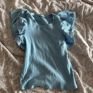 Blå ribbad topp med volangärmar - Supersöt ljusblå topp med ribbad struktur och stora volangärmar som ger en extra touch.