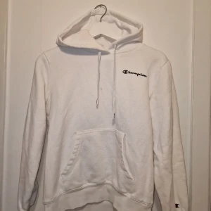 Vit hoodie från Champion - Vit hoodie från Champion i storlek medium. Mjuk och skön bomullsmix, perfekt för chill eller streetwear. Har en liten fläck på framsidan (se första bilden) annars i väldigt fint skick. Passar även S.