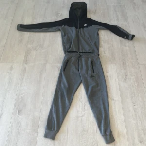 Grå och svart Nike teck full set byxor och överdel - Snyggt grå svart Nike teck set i bra skick båda är i storlek S.snöret på byxorna är det enda problemet som inte stör