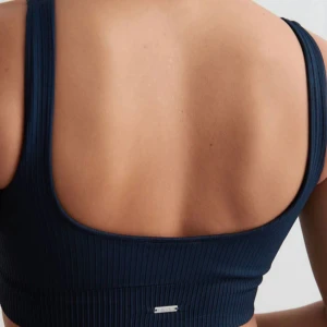 Mörkblå ribbad linnetopp Aim'n S - Supersnygg mörkblå ribbad linnetopp från Aim'n i seamless design. Ny med prislapp. Toppen har breda axelband, croppad passform och ett metallmärke framtill. Perfekt för träning eller chill. Materialet är mjukt och stretchigt syntet som sitter skönt mot kroppen.