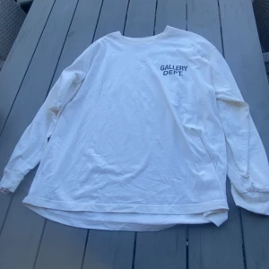 Vit långärmad tröja Gallery Dept. - Vit långärmad tröja från Gallery Dept. med tryck på bröstet och ryggen. Tröjan har en rund hals och är gjord i mjuk bomull, perfekt för chill dagar. Oversized passform för en avslappnad vibe. Snyggt tryck med 'HOLLYWOOD, CA' på ryggen.