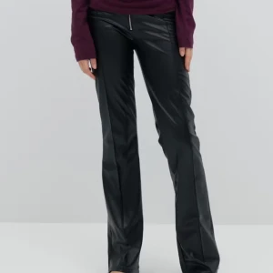 Lågmidjade Skinnbyxor  - Snygga svarta byxor med bootcut passform och låg midja i skinnimitation. De har en markerad dragkedja framtill och breda benslut som ger en cool siluett. Perfekta för dig som vill sticka ut med en edgy vibe. Passar till både sneakers och boots.