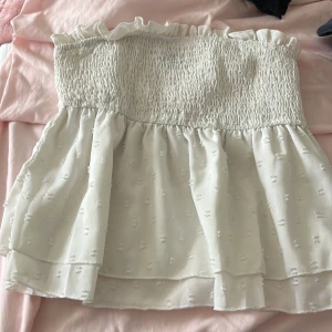 Vit bandeau tubtopp från SHEIN - Supersöt vit bandeau tubtopp från SHEIN med volangkant upptill och smockad överdel. Toppen har ett skirt lager med små broderade prickar och är helt axelbandslös. Perfekt för sommarens alla häng och selfies!