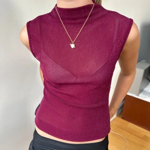 Glittrig vinröd ärmlös polotopp - Säljer en glittrig vinröd polotopp med ärmlös design. Toppens material är tunn och lätt transparent med en snygg glansig finish. Hög hals ger en trendig look och den sitter tajt mot kroppen. Perfekt för dig som vill sticka ut med en cool och modern vibe.