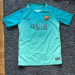 Barcelona Neymar Jr fotbollströja  - Snygg Barcelona fotbollströja från Nike med Neymar Jr och nummer 11 på ryggen. Tröjan är turkos med tunna svarta ränder, har korta ärmar och är gjord i lätt Dri-Fit material. Framsidan har klubbmärke och Qatar Airways-logga, baksidan har UNICEF-tryck.