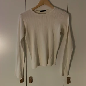 Vit ribbad långärmad tröja Brandy Melville - Säljer en vit långärmad tröja från Brandy Melville med ribbad struktur och diskreta små hålmönster. Tröjan har rund hals och är gjord i mjuk bomull, perfekt för dig som gillar clean och enkel stil. Passar dig som vill ha en basic men ändå söt topp.