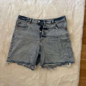 90's cutoff jeansshorts från H&M - Snygga ljusblå jeansshorts från H&M med hög midja och råa, fransiga kanter. Klassisk femficksmodell med knappgylf och vintageinspirerad tvätt. Perfekta för en chill sommardag och har en loose fit som ger skön streetkänsla.