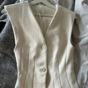 Vit tröja  från Zara med knappar - Snygg vit tröja från Zara i storlek S. Tröjan  har en stilren design med två knappar framtill och markerade sömmar som ger en schysst form. Materialet känns mjukt och har en lätt struktur. 