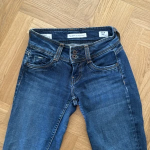 Blå jeans med dubbla knappar och låg midja - Säljer ett par klassiska blå jeans med snygg tvätt och dubbla knappar i midjan. Jeansen har raka ben, fem fickor och detaljerade sömmar. Perfekt för dig som gillar en tidlös look med lite edge. Skicka DM om du vill veta mer!