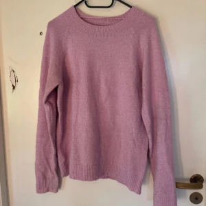 Ljusrosa stickad tröja - Mysig ljusrosa stickad tröja med rund hals och långa ärmar. Tröjan har ribbade muddar vid hals, ärmslut och nederkant, vilket ger en skön och avslappnad passform. Perfekt för kyliga dagar när du vill vara både bekväm och snygg.