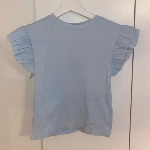 Ljusblå ribbad topp med volangärmar - Supersöt ljusblå topp från Gina Tricot i ribbad bomull. Toppen är i storlek 158-164 i Gina Young men passar också storlek xs.